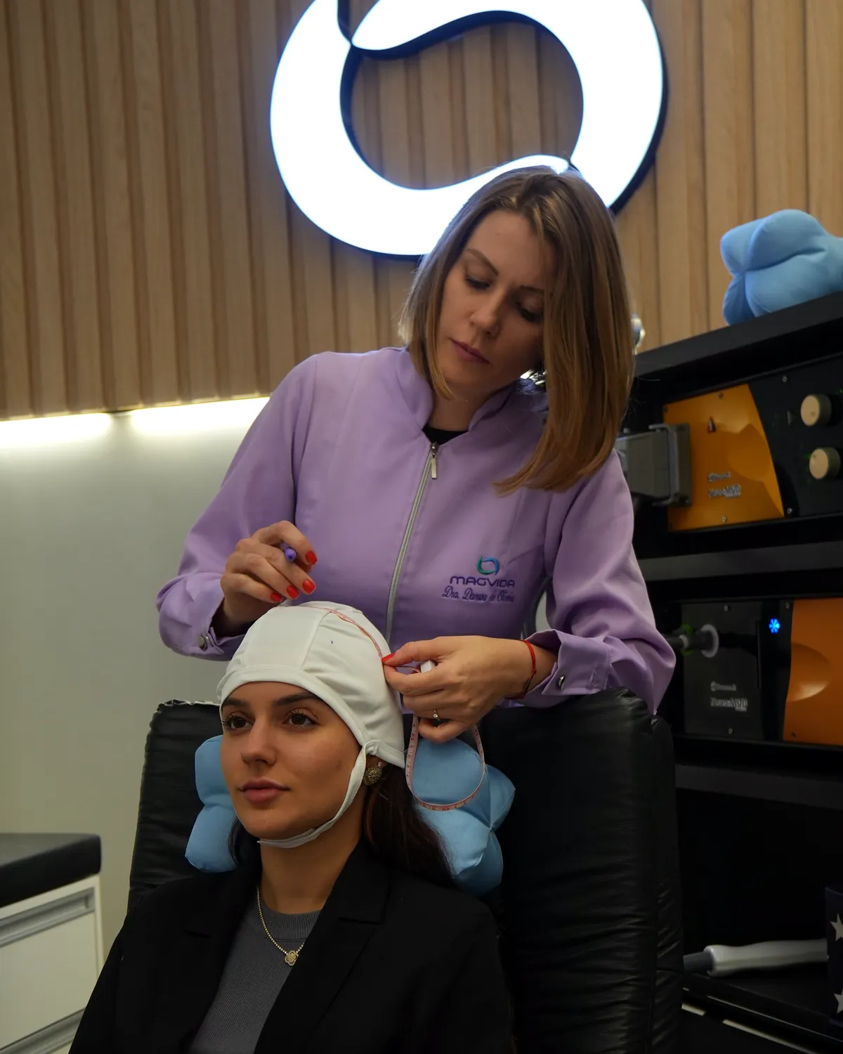 Fisioterapeuta ajustando a touca de marcação na cabeça da paciente